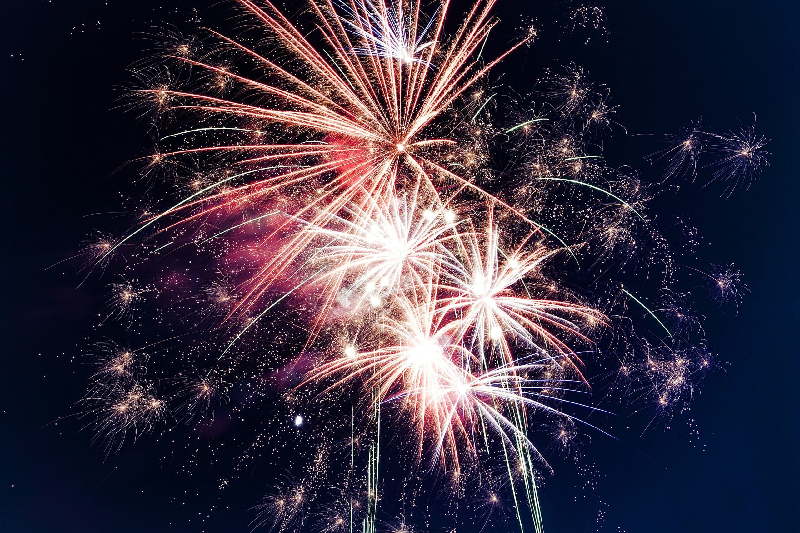 A photo of pink and orange fireworks on a dark blue night sky background.