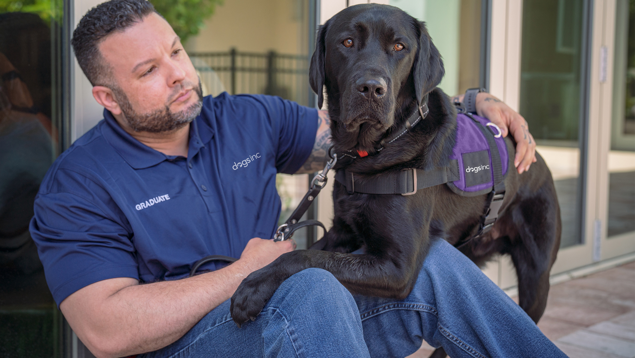 A man sits on the ground as his service dog sets it's paw on his lap