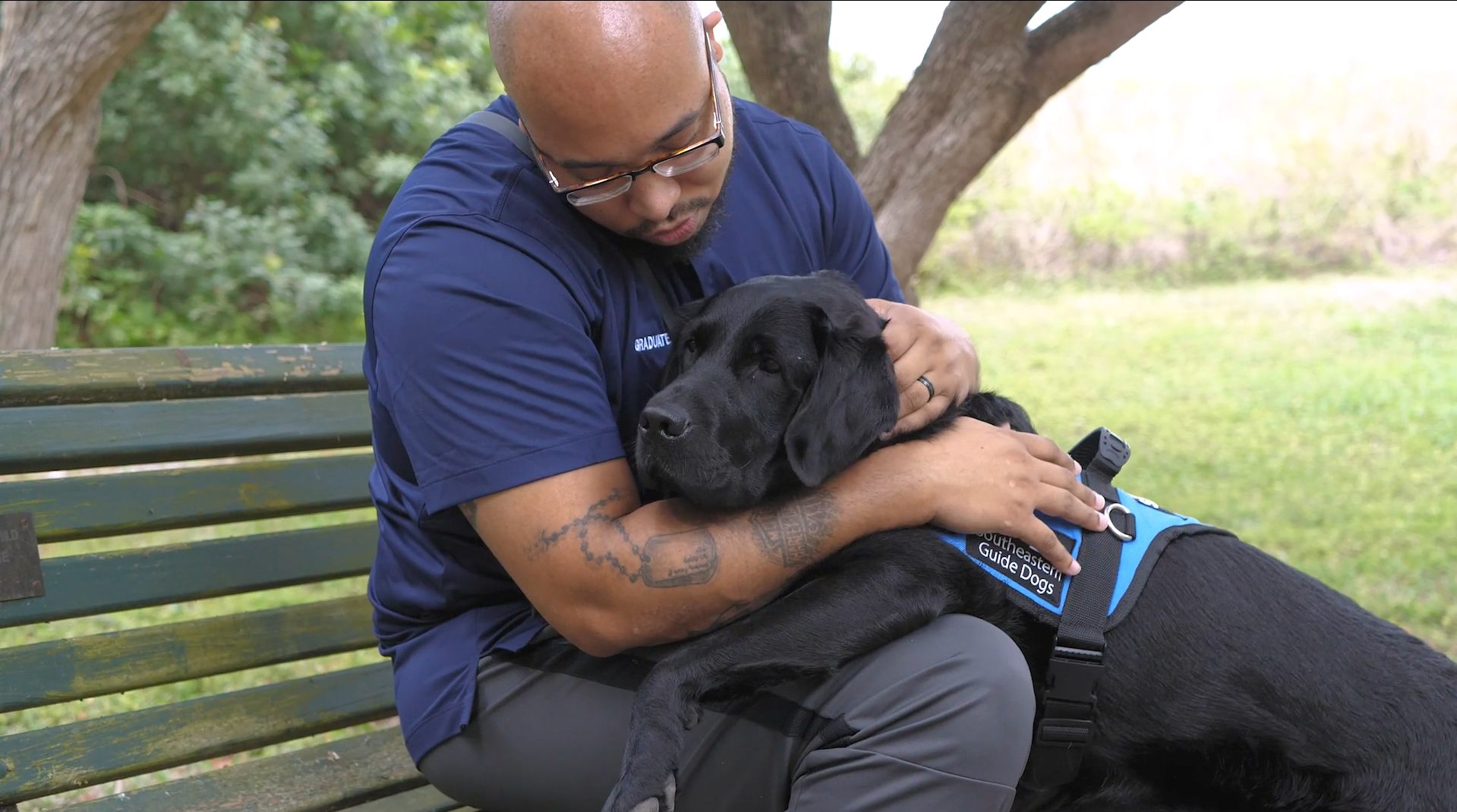 Veteran man sits on bench with black service dog on his lap