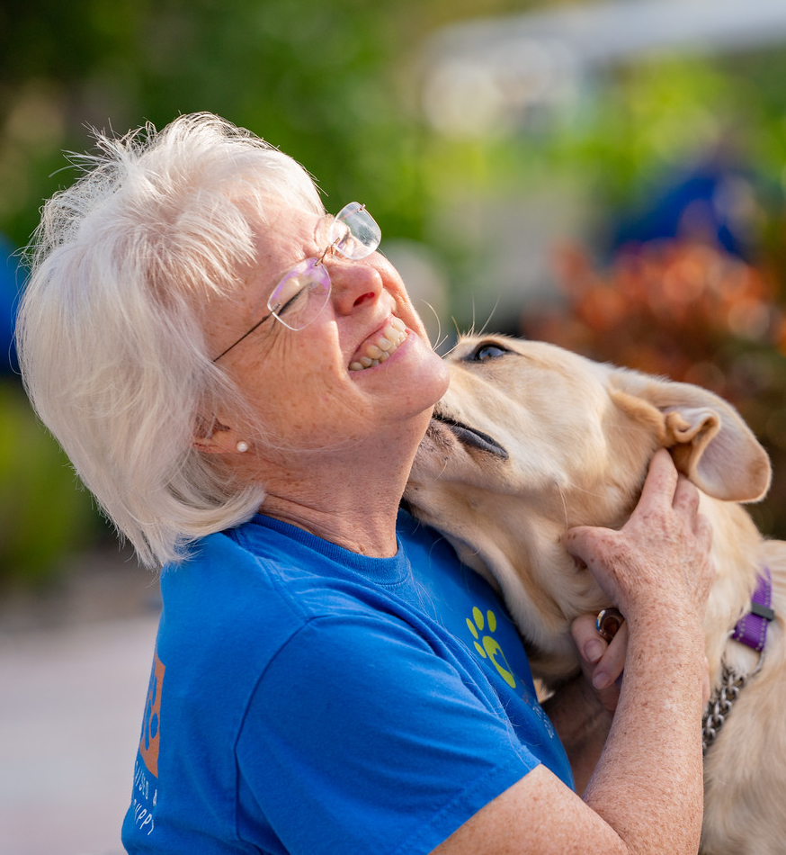 Older woman laughs while yellow puppy gives kiss on her neck