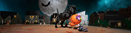 A black Labrador Retriever puppy leaping with a pumpkin treat-or-treat bucket in her mouth.