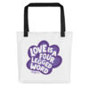 A white tote bag with 'Love is a Four Legged Word' text inside a purple paw print graphic.