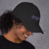 The right side profile of a black dad hat with the Dogs Inc logo embroidered in purple and blue.