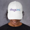 A white dad hat with the Dogs Inc logo embroidered in purple and blue.