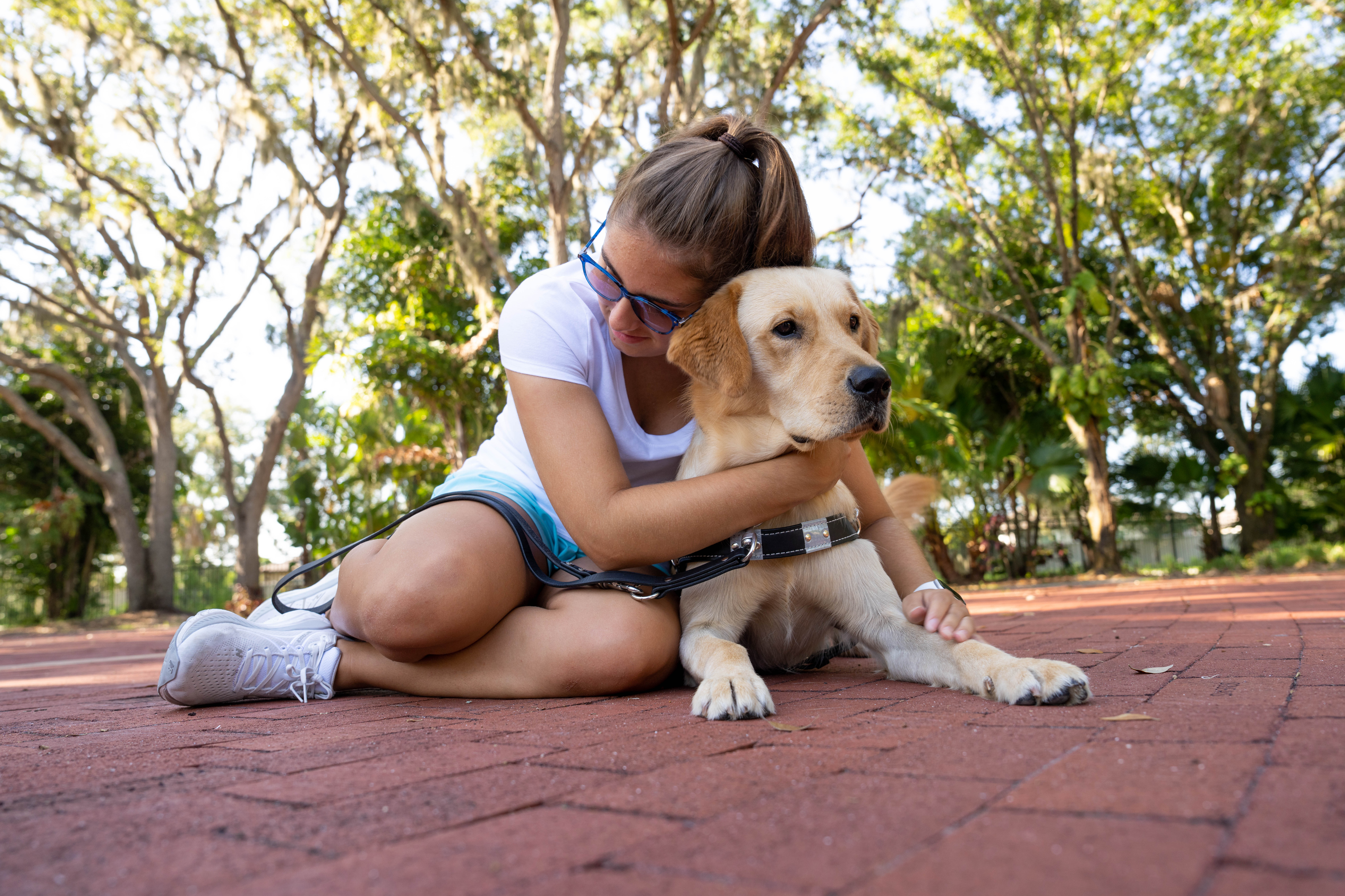 A female cuddles her yellow Labrador guide dog.