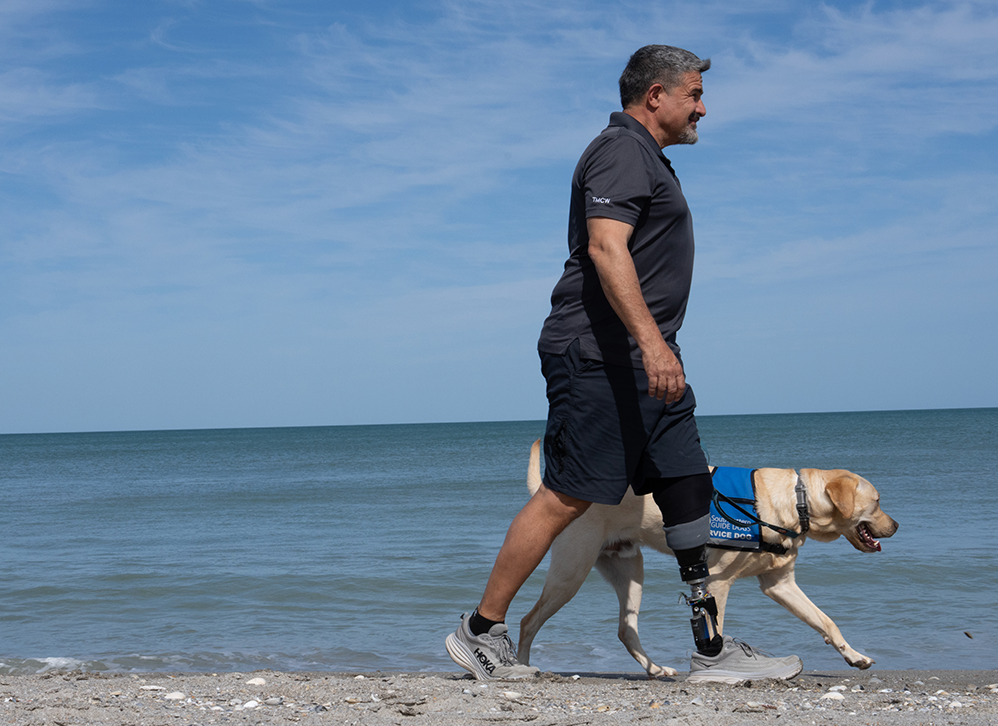 John Alvarez walks with his yellow Labrador service dog on the beach.