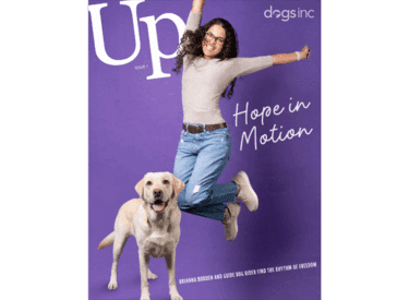 White text reads Up and Dogs Inc. A woman jumps for joy next to white text that reads "Hope in Motion." A yellow Labrador guide dog stands next to her.