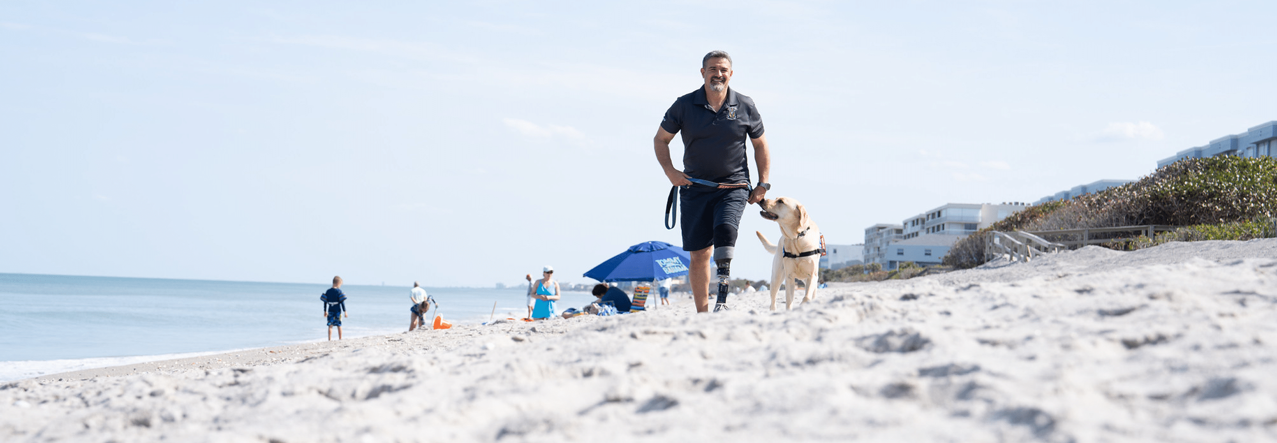 A man with a prosthetic leg confidently dormitories alongside a Labrador Retriever at the beach.